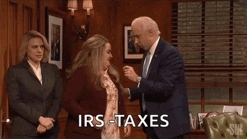 a man in a suit and tie is standing next to two women in a room and says `` irs taxes '' .