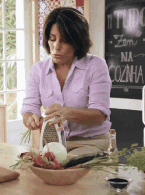 a woman is grating onions in front of a sign that says tudo na cozinha