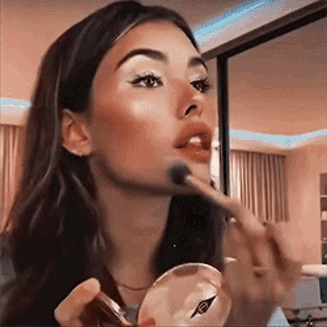 a woman is applying powder to her face with a brush .
