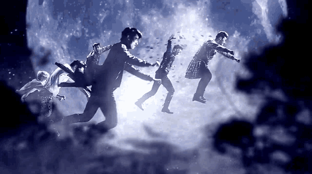 a group of people are dancing in front of a large moon