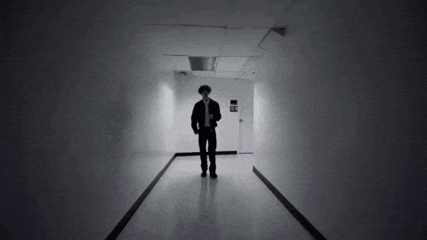 a man is walking down a hallway in a dark room holding a cell phone .