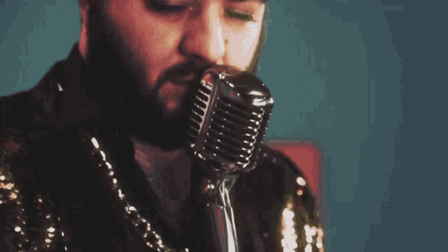 a man with a beard is singing into a microphone and looking at the camera