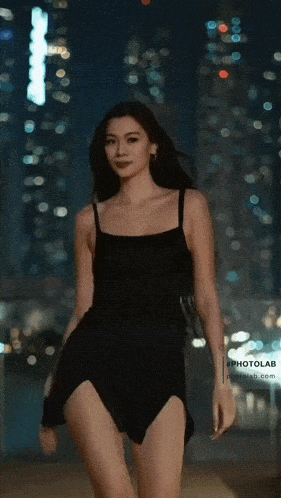 a woman in a black dress is walking in front of a city skyline