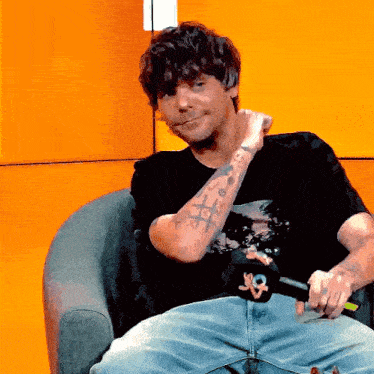 a man with a tattoo on his arm is sitting in a chair holding a microphone ..