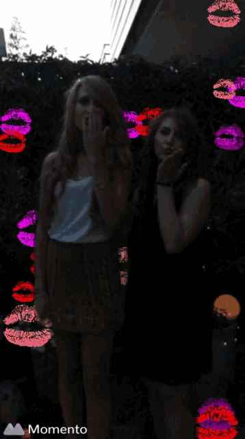 two women blowing kisses in front of a wall of kisses with the word momento on the bottom