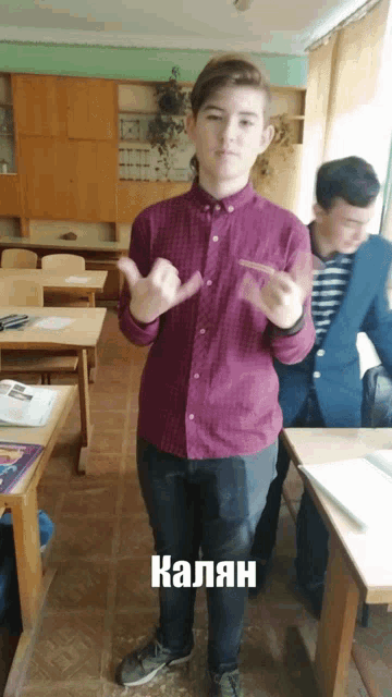 a young man in a purple shirt is standing in a classroom with the word kaliah written on the floor