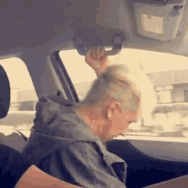 a woman is sitting in the driver 's seat of a car with her hand on the rear view mirror .