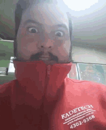 a man with a beard and mustache is wearing a red jacket that says kadetech .