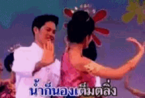 a man and a woman are dancing in front of a sign that says ' น้ํา กับ อง ' on it