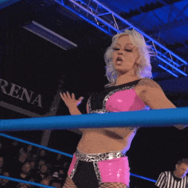 a woman in a pink and black outfit stands in a wrestling ring