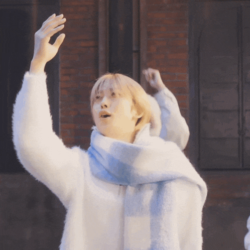 a person wearing a white sweater and a blue scarf holds their hands up in the air