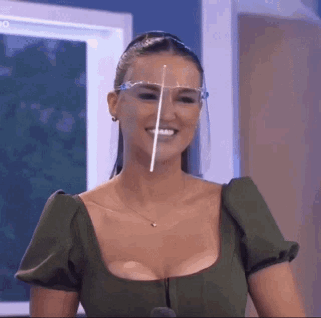 a woman is wearing a face shield and smiling while standing in front of a microphone .