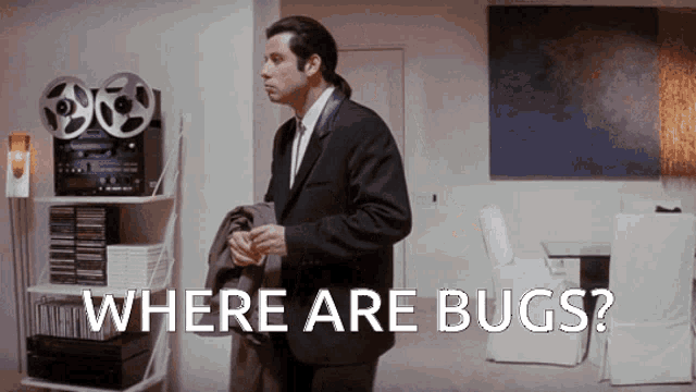 a man in a suit and tie is standing in a living room with the words " where are bugs " on the screen