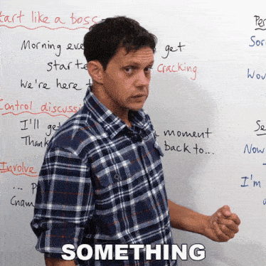 a man in a plaid shirt stands in front of a white board with the words something written on it