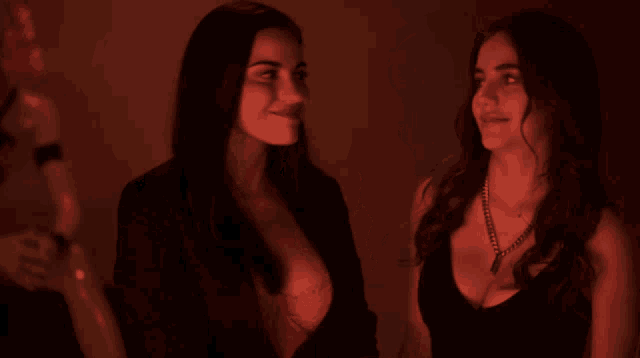 two women are standing next to each other in a dark room and one has a bra on