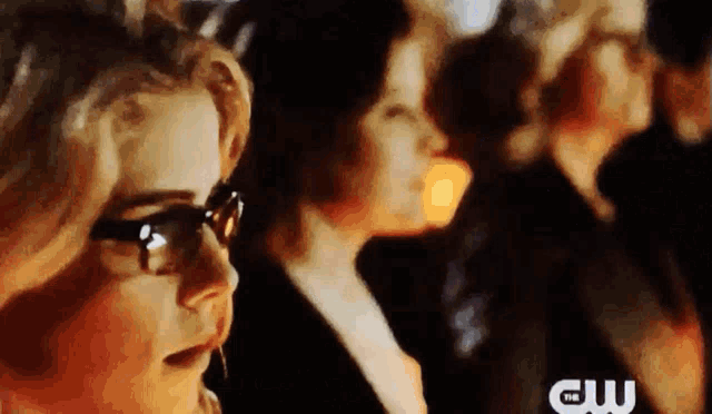 a close up of a woman wearing glasses standing next to a group of women .