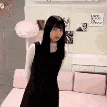 a woman in a black dress is standing in front of a pink couch in a room .