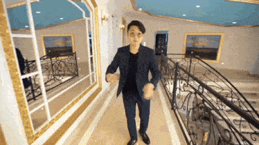 a man in a suit is walking down a hallway with a wrought iron railing .