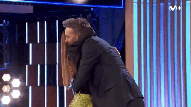 a man in a suit is hugging a woman on a stage with the letter m on the bottom right