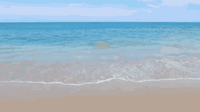 a beach with waves crashing on the sand and a blue sky in the background
