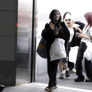 a group of people are walking out of an elevator and a woman is holding a bag .