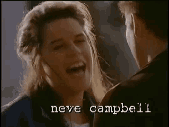 a woman laughs while looking at a man with the name neve campbell on the bottom right