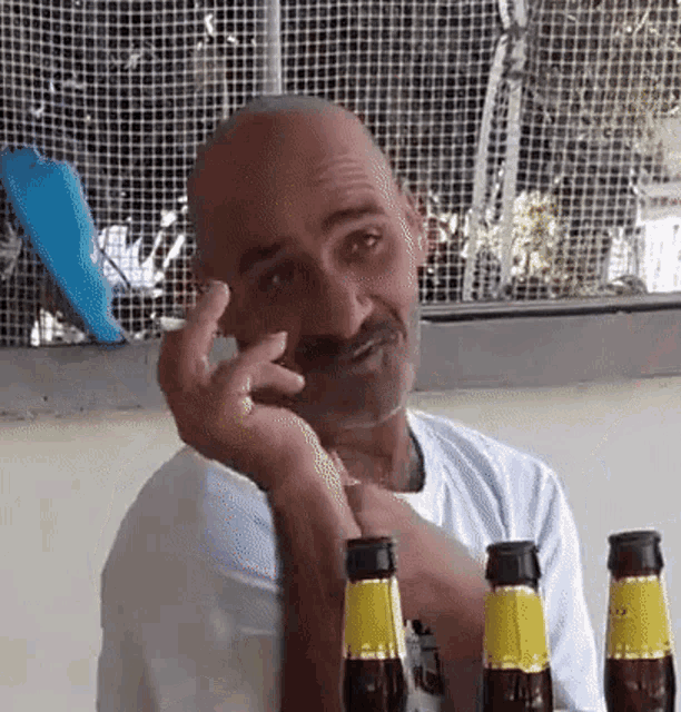 a man is sitting at a table with three bottles of beer and talking on a cell phone .