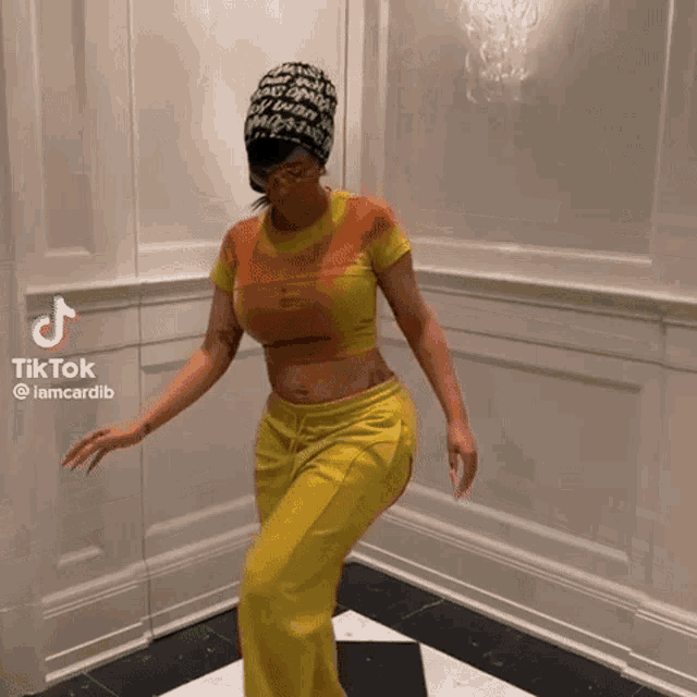 a woman is dancing in a room wearing yellow pants and a hat .
