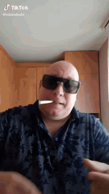 a man wearing sunglasses is smoking a cigarette in a kitchen .