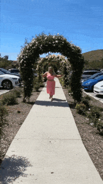 a woman in a pink dress is running under a rose arch