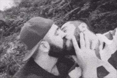 a man in a hat is kissing another man on the cheek