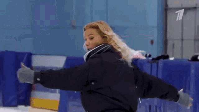 a woman in a black jacket is standing on a ice rink with a tv logo on the wall behind her