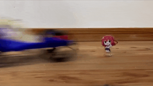 a toy girl is standing on a wooden floor in front of a blue toy car .