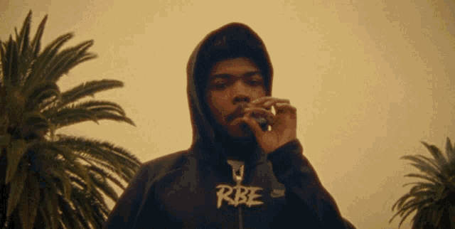a man wearing a hoodie with the word rbe on it smoking a cigarette