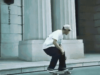 a man in a white shirt is riding a skateboard on a sidewalk