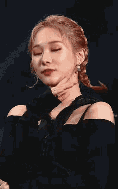 a close up of a woman 's face with her hand on her chin . she is wearing a black top and earrings .