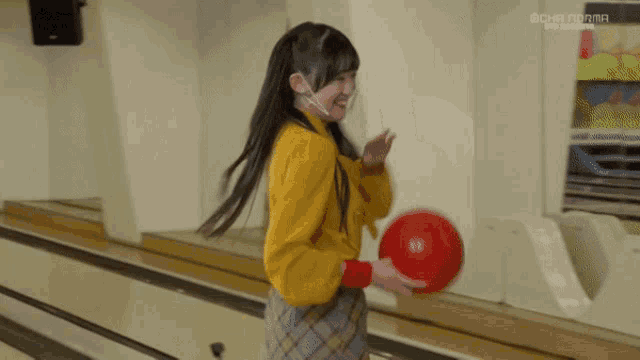 a girl in a yellow shirt is holding a red bowling ball on a bowling alley