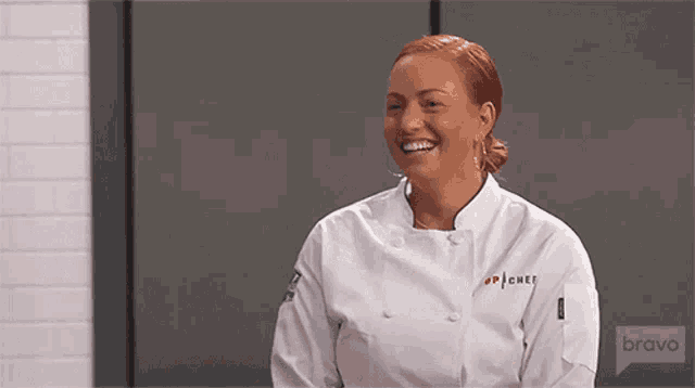 a woman in a chef 's uniform is smiling while sitting in front of a wall .