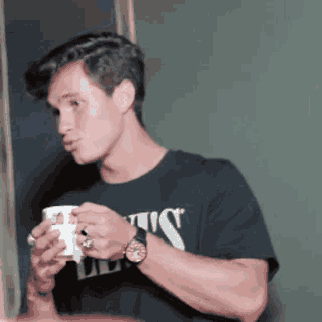 a man wearing a t-shirt that says ' us ' on it is holding a cup of coffee