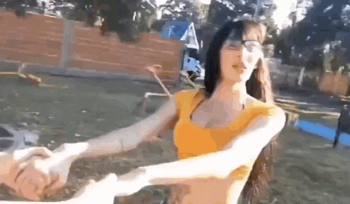 a woman in a yellow tank top is holding another woman 's arm in a park .