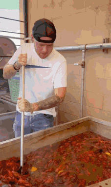a man with a tattoo on his arm is holding a stick over a large container of crawfish