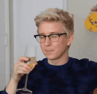 a man wearing glasses is holding a glass of wine and making a funny face .