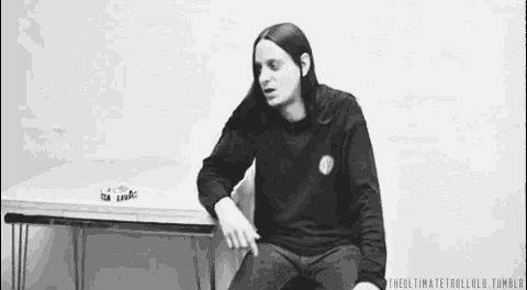 a man with long hair is sitting in a chair in front of a table in a black and white photo .