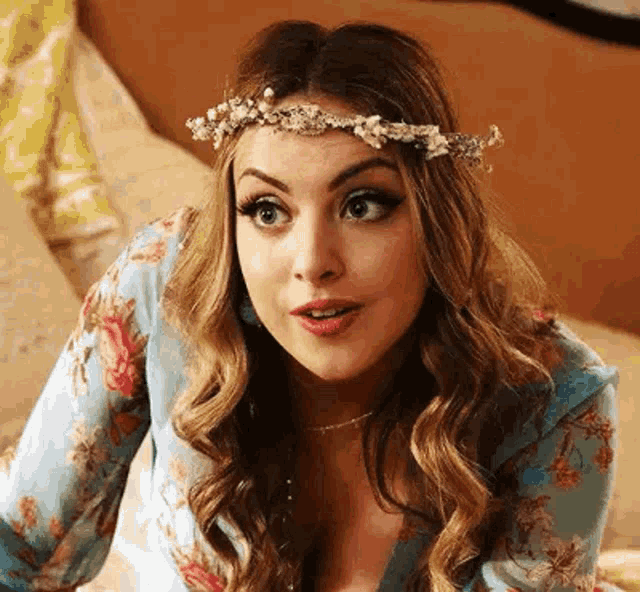 a woman wearing a flower crown is sitting on a bed and making a funny face .