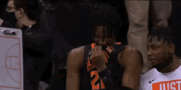 a basketball player is sitting in the stands with his hands on his chest and laughing .