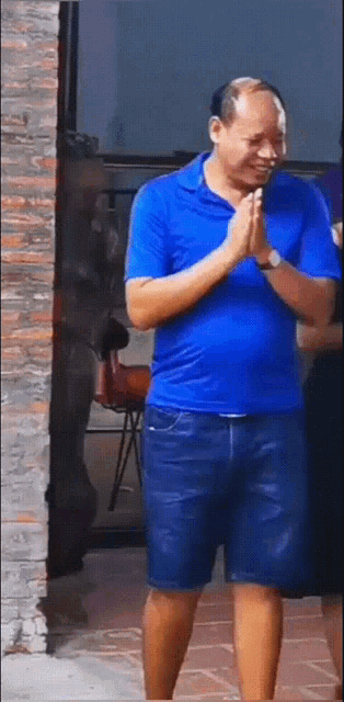 a man in a blue shirt and shorts is praying with his hands together