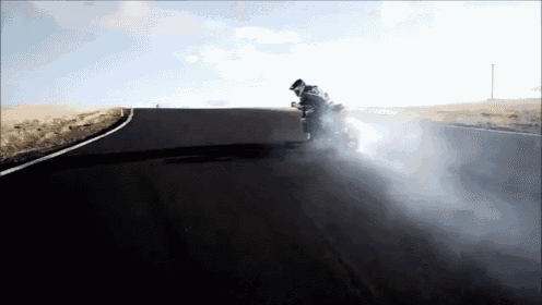 a person is riding a motorcycle down a road with smoke coming out of the tire