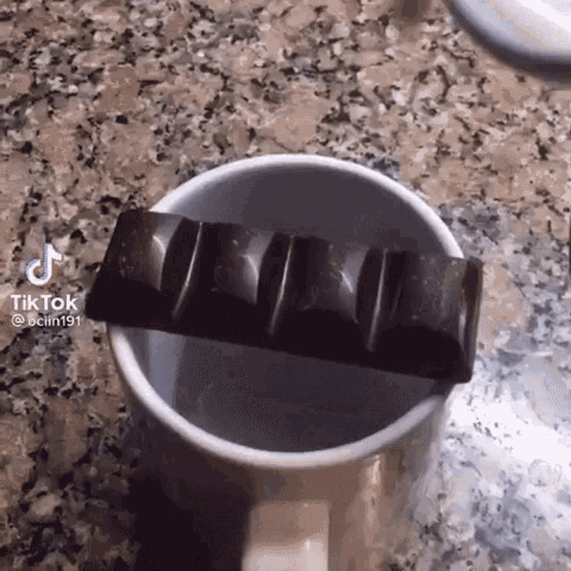 a bar of chocolate is sticking out of a mug on a counter .