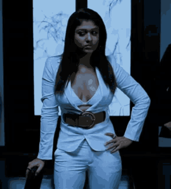 a woman in a white suit with a plunging neckline is standing in front of a window .