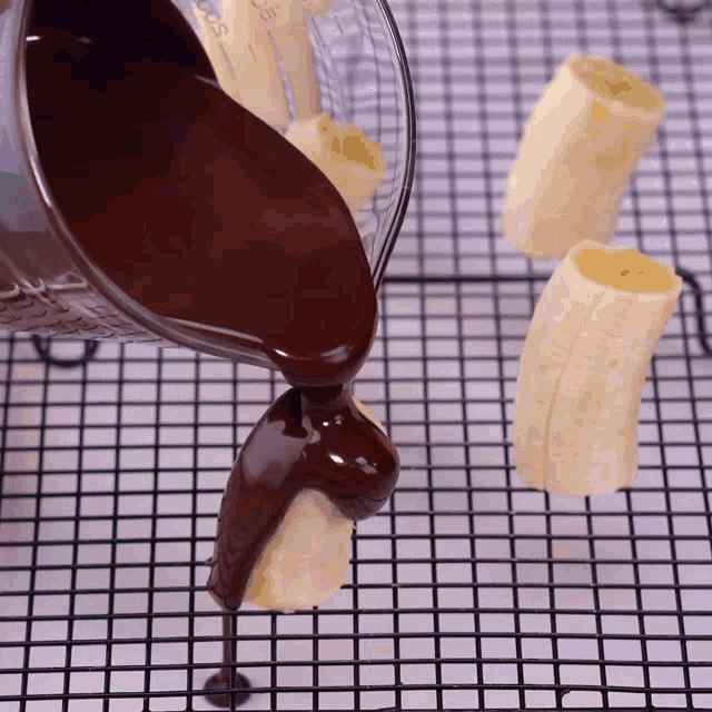 a measuring cup filled with chocolate is being poured over sliced bananas on a cooling rack